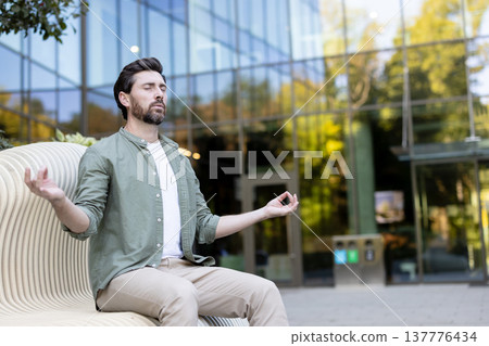 Man practicing mindfulness meditation in lotus position on a modern park bench, finding peace and balance amidst an urban building background, promoting mental wellness and healthy lifestyle Man practicing mindfulness meditation in lotus position on a modern park bench, finding peace and balance amidst an urban building background, promoting mental wellness and healthy lifestyle 137776434