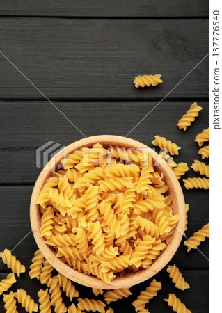Bowl of raw fusilli pasta on black wooden background. Vertical photo 137776540