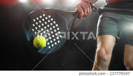Dynamic action shot of a padel player hitting a yellow ball with a racket during a match. Dramatic lighting highlights movement, speed and power, capturing the energy and intensity of modern racket 137776597