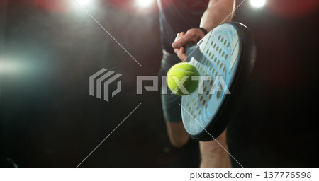 Dynamic action shot of a padel player hitting a yellow ball with a racket during a match. Dramatic lighting highlights movement, speed and power, capturing the energy and intensity of modern racket 137776598