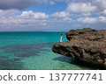A woman on a rocky outcrop gazing at the emerald sea. 137777741