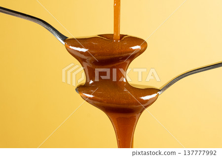 Two spoons with dripping caramel sauce in motion. 137777992