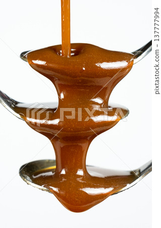Flowing stream of liquid caramel on white background. Flowing stream of liquid caramel on white background. 137777994
