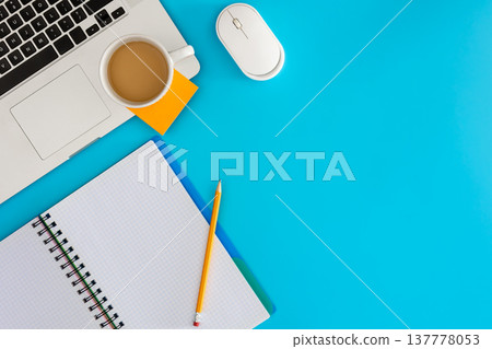 Laptop with notebook and cup of coffee on blue background. 137778053