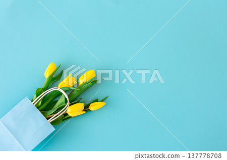 Flat lay blue background with yellow tulip flowers in a paper bag. Flat lay blue background with yellow tulip flowers in a paper bag. 137778708