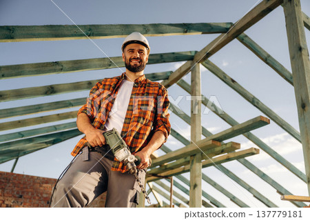 The drill is in hands. Construction worker is on the roof of a house The drill is in hands. Construction worker is on the roof of a house 137779181
