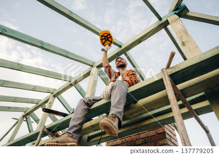 Friendly man is sitting and taking a break. Construction worker is on the roof of a house 137779205