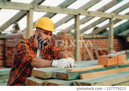 Measuring the length of plank. Construction worker is on the roof of a house Measuring the length of plank. Construction worker is on the roof of a house 137779223