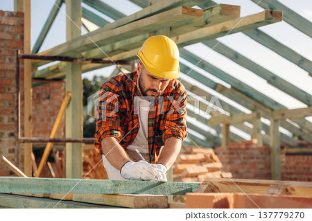 Measuring and marking the plank. Construction worker is on the roof of a house Measuring and marking the plank. Construction worker is on the roof of a house 137779270