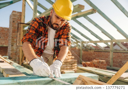 Measuring and marking the plank. Construction worker is on the roof of a house Measuring and marking the plank. Construction worker is on the roof of a house 137779271