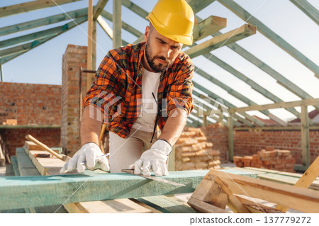 Measuring and marking the plank. Construction worker is on the roof of a house Measuring and marking the plank. Construction worker is on the roof of a house 137779272