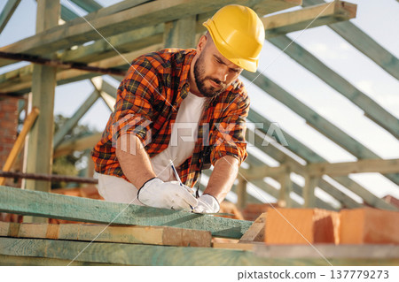 Measuring and marking the plank. Construction worker is on the roof of a house Measuring and marking the plank. Construction worker is on the roof of a house 137779273
