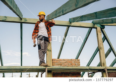 Unfinished place, under sunlight. Construction worker is on the roof of a house 137779297