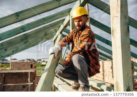 Unfinished place, under sunlight. Construction worker is on the roof of a house Unfinished place, under sunlight. Construction worker is on the roof of a house 137779306