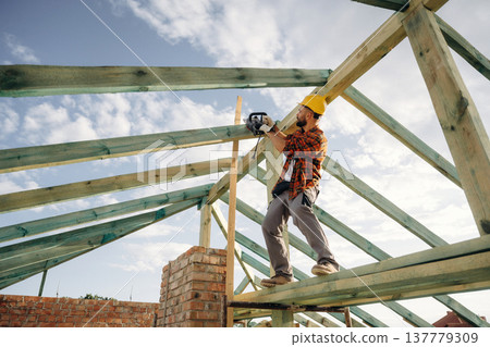 Engineer is high up with chainsaw. Construction worker is on the roof of a house Engineer is high up with chainsaw. Construction worker is on the roof of a house 137779309