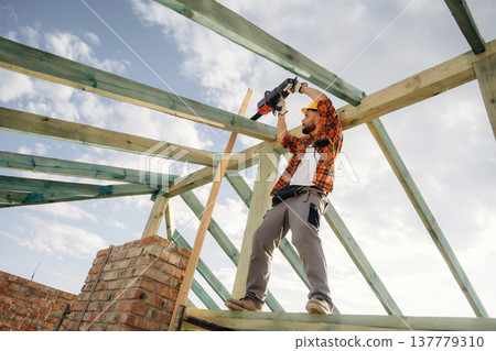 Engineer is high up with chainsaw. Construction worker is on the roof of a house Engineer is high up with chainsaw. Construction worker is on the roof of a house 137779310