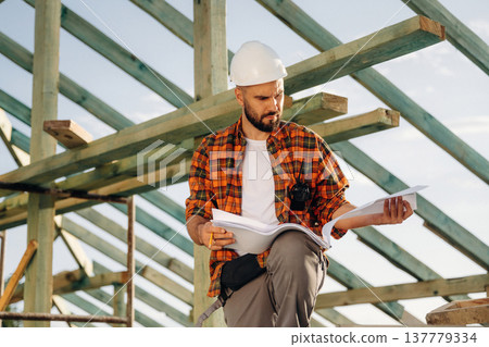 With a plan on paper. Construction worker is on the roof of a house 137779334