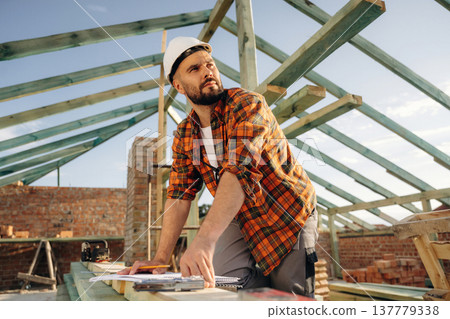 With a plan on paper. Construction worker is on the roof of a house With a plan on paper. Construction worker is on the roof of a house 137779338