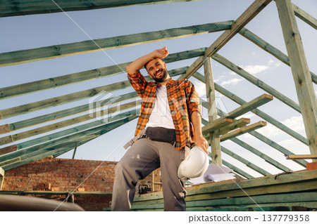 Tired, taking a break. Construction worker is on the roof of a house 137779358