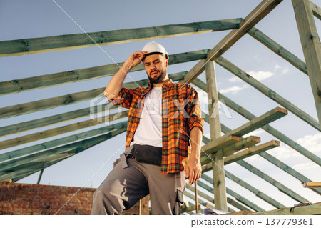 Tired, taking a break. Construction worker is on the roof of a house Tired, taking a break. Construction worker is on the roof of a house 137779361