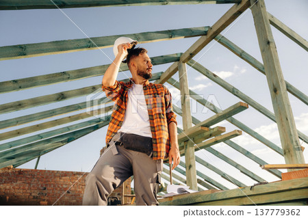 Tired, taking a break. Construction worker is on the roof of a house Tired, taking a break. Construction worker is on the roof of a house 137779362