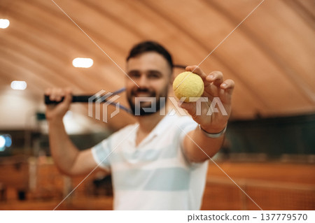 Holding and showing ball. Man is playing tennis indoors in the hangar 137779570