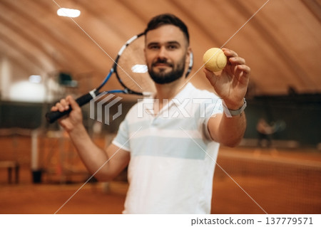 Showing tennis ball that is in hand. Man is indoors in the hangar 137779571