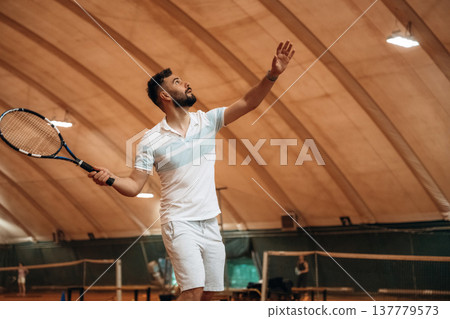 Side view, game in action. Man is playing tennis indoors in the hangar Side view, game in action. Man is playing tennis indoors in the hangar 137779573