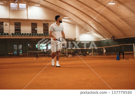 Holding racket, active. Man is playing tennis indoors in the hangar 137779580