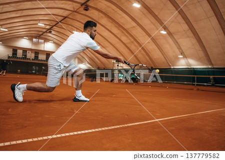 Holding racket, active. Man is playing tennis indoors in the hangar 137779582