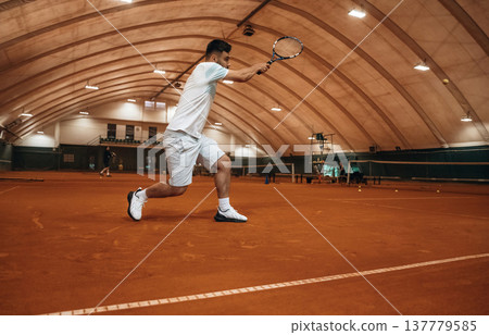 Running with racket, active time spending. Man is playing tennis indoors in the hangar 137779585