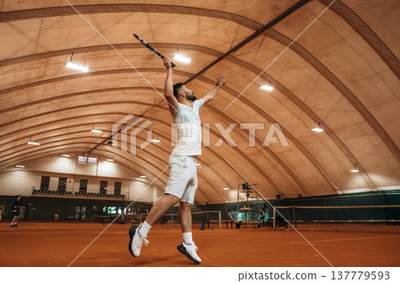 Jumping, photo in action. Man is playing tennis indoors in the hangar 137779593
