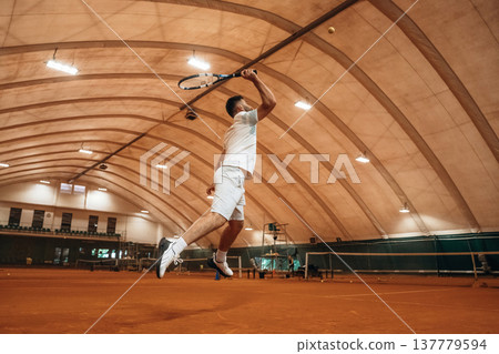 In the air, jumping. Man is playing tennis indoors in the hangar 137779594