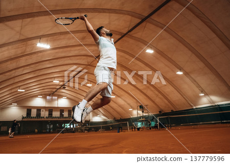 In the air, jumping. Man is playing tennis indoors in the hangar 137779596