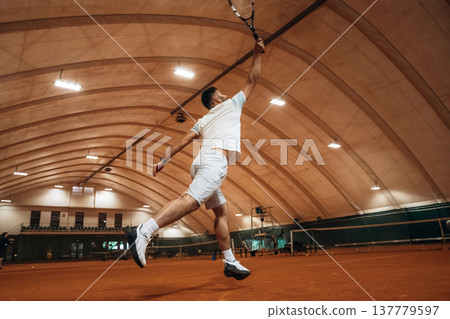 In the air, jumping. Man is playing tennis indoors in the hangar 137779597
