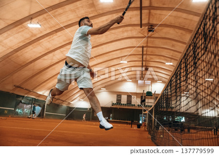 In the air, jumping. Man is playing tennis indoors in the hangar 137779599