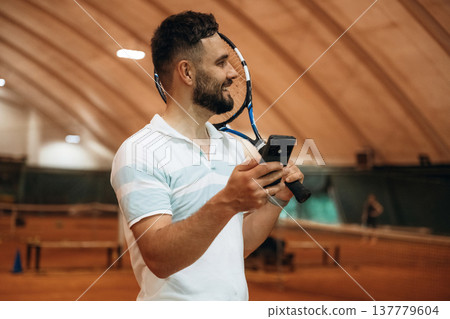 Smartphone is in hand. Man is playing tennis indoors in the hangar Smartphone is in hand. Man is playing tennis indoors in the hangar 137779604