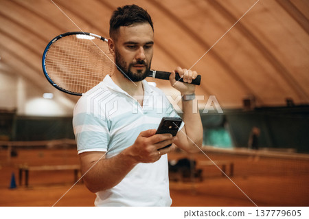Smartphone is in hand. Man is playing tennis indoors in the hangar 137779605