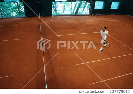 Top down view. Man is playing tennis indoors in the hangar Top down view. Man is playing tennis indoors in the hangar 137779613