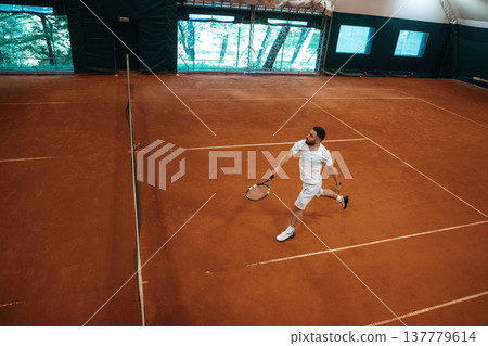 Top down view. Man is playing tennis indoors in the hangar Top down view. Man is playing tennis indoors in the hangar 137779614