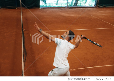 In white sport clothes. Man is playing tennis indoors in the hangar 137779622