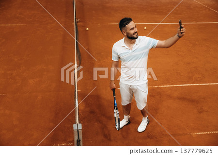 Smartphone is in hand. Man is playing tennis indoors in the hangar 137779625