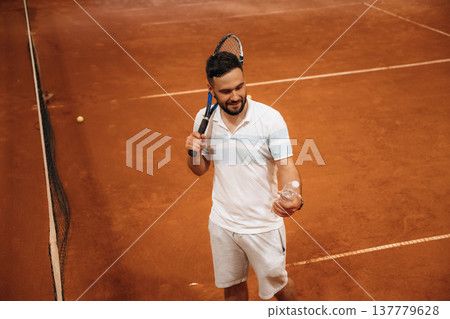 Taking break, with bottle of water. Man is playing tennis indoors in the hangar 137779628
