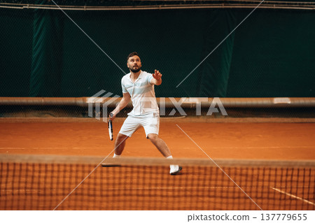 Front view. Man is playing tennis indoors in the hangar Front view. Man is playing tennis indoors in the hangar 137779655