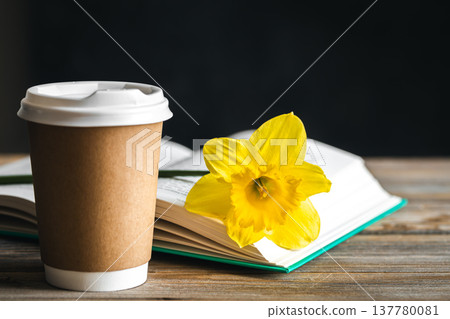 Paper cup, book and yellow flower on a blurred wooden background. 137780081