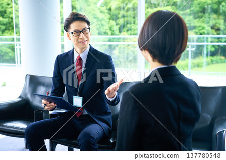 一位面帶笑容的商人和一位女士在明亮的休息室裡進行商務洽談並提出方案。 137780548