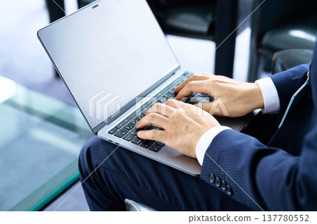 A businessman's hands typing on a laptop on his lap. A businessman's hands typing on a laptop on his lap. 137780552
