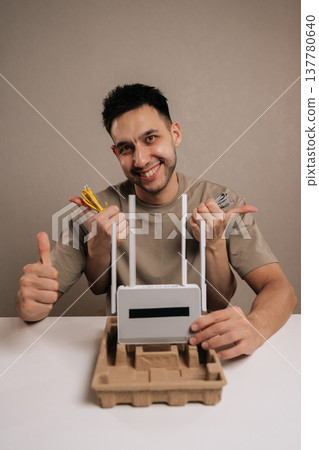 Vertical portrait of enthusiastic man setting up new wireless internet router, holding essential ethernet cables and network adapter for home connectivity, smiling looking camera, isolated background. Vertical portrait of enthusiastic man setting up new wireless internet router, holding essential ethernet cables and network adapter for home connectivity, smiling looking camera, isolated background. 137780640