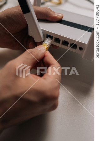 Closeup hand of technician plugging ethernet cable into wireless internet router, creating stable network connection for data transmission and digital communication in computing environment. Closeup hand of technician plugging ethernet cable into wireless internet router, creating stable network connection for data transmission and digital communication in computing environment. 137780643