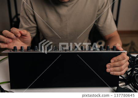 Close-up of audio engineer hands adjusting controls on sound mixer, working with audio equipment in a professional music studio, focusing on sound production and creative mixing. 137780645